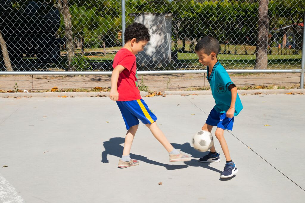 Levi plays soccer on a basketball court with a friend.